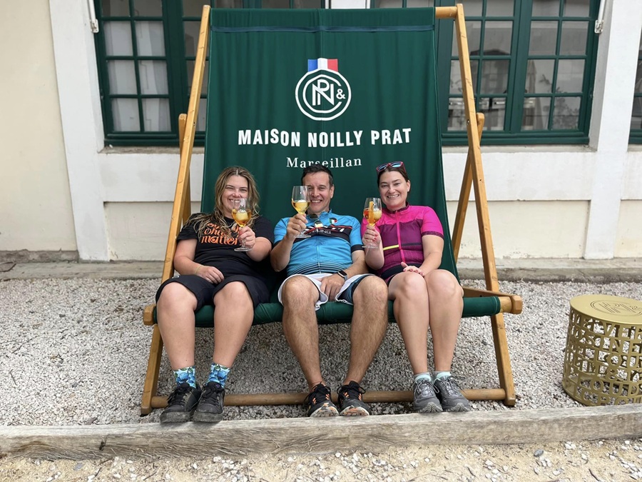 Three cyclists relax in a huge Noilly Prat deckchair with glasses in their hands